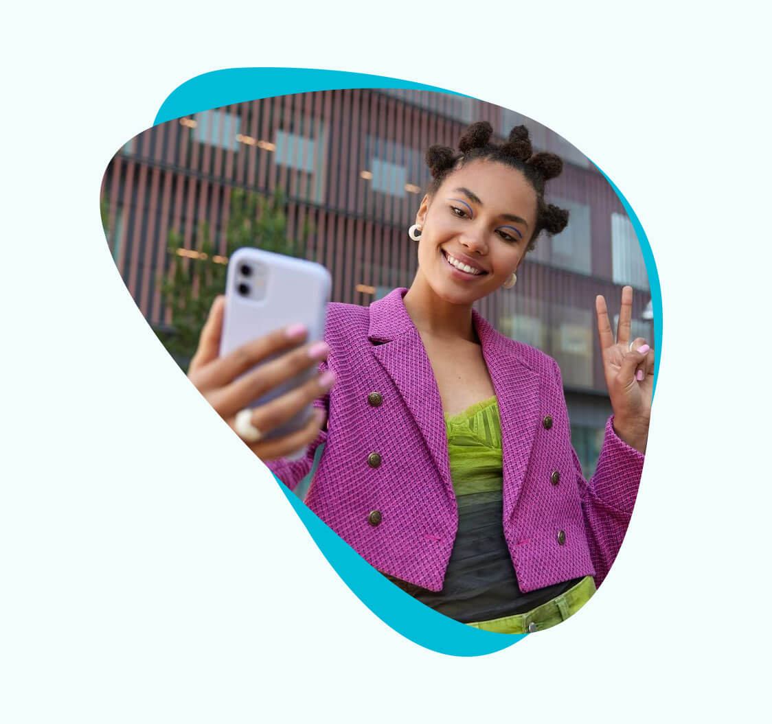 A young influencer taking a selfie with her smartphone. She's holding up two fingers on her left hand and smiling.